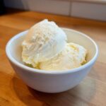 Two scoops of creamy, vanilla-colored protein ice cream served in a small white bowl.