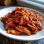 Close-up of richly sauced, shredded chicken tinga piled high on a white plate.