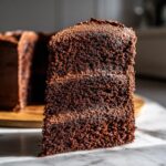 Close-up of a thick slice of homemade chocolate cake showing its dark, moist crumb and layer of frosting.