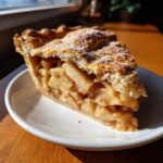 Close-up of a thick slice of homemade apple pie showing chunky filling and a flaky crust sprinkled with sugar.
