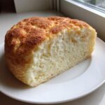 A thick slice of light, airy cloud bread with a golden-brown, textured top, served on a white plate.