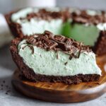 Close-up of a slice of grasshopper pie featuring a dark chocolate crust and light green mint filling topped with chocolate shavings.