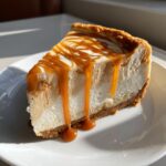 A decadent slice of creamy salted caramel cheesecake topped with thick caramel drizzle dripping down the side.
