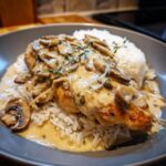 A serving of smothered chicken and rice topped with creamy mushroom gravy and fresh thyme.