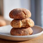 A stack of three soft, round applesauce cookies coated in cinnamon sugar, with the middle cookie broken open.