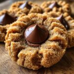 A close-up of a freshly baked, sugar-coated peanut butter blossom cookie with a melted chocolate kiss center.