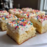Close-up of soft sugar cookie bars topped with thick white frosting and colorful sprinkles.