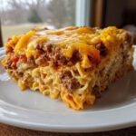 A generous slice of sour cream beef noodle casserole topped with melted cheddar cheese on a white plate.