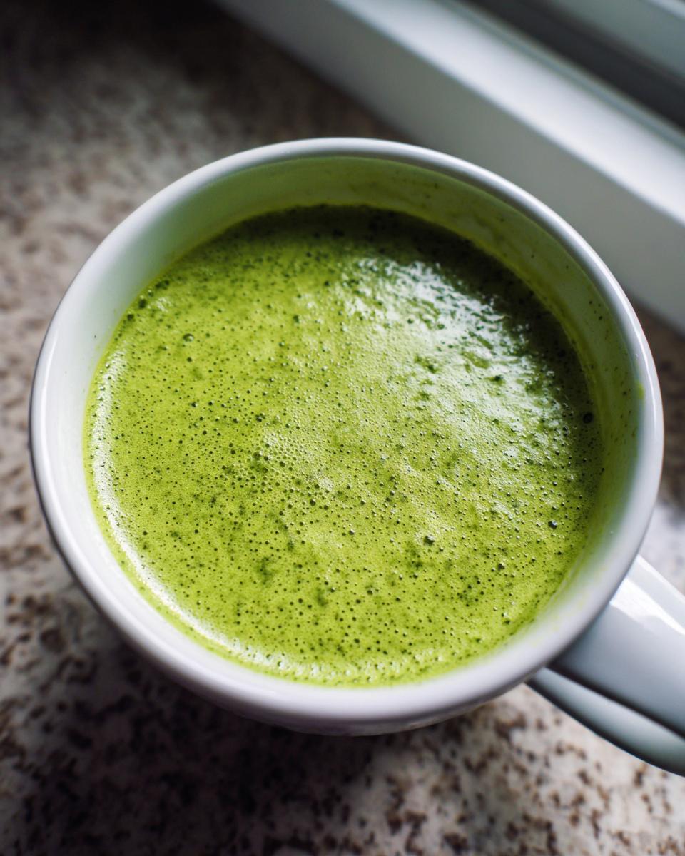 Close-up overhead view of bright green, frothy spinach soup served in a white mug.