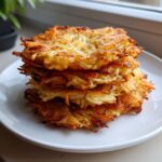 A tall stack of five golden-brown, crispy potato pancakes served on a white plate.