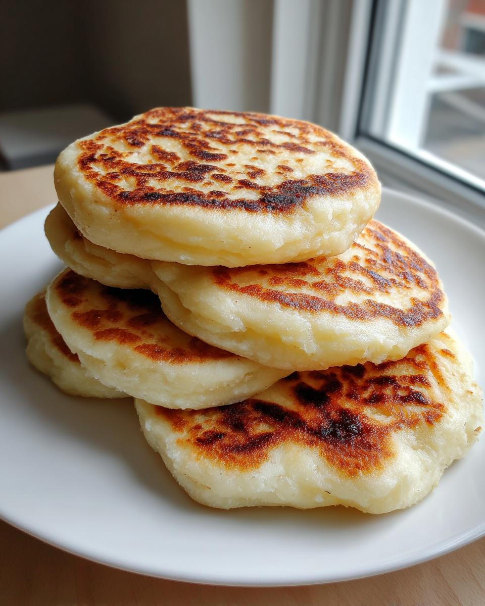 A stack of freshly cooked, round Irish potato farls with golden brown, slightly charred tops served on a white plate.