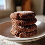 A stack of four rich, dark brown soft gingerbread cookies generously coated in sparkling white sugar crystals.