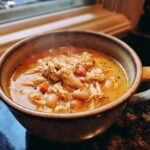 Close-up of a steaming bowl of creamy white chicken chili, featuring shredded chicken, white beans, and carrots.