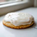 A single, round sugar cookie topped with thick, glossy white sugar cookie icing recipe frosting and tiny white sprinkles.