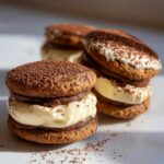 Three stacked tiramisu cookies filled with rich cream and dusted heavily with cocoa powder.