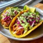 Close-up of two loaded salmon tacos topped with purple cabbage slaw and creamy green sauce.