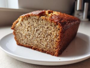 Close-up of a thick slice of moist vegan banana bread showing its speckled crumb texture on a white plate.