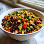 Close-up of a white bowl filled with colorful cowboy caviar featuring black beans, corn, red peppers, and cilantro.