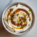 Overhead view of a bowl of creamy whipped feta dip swirled and topped with chopped pistachios and a drizzle of honey.