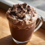 A close-up of rich whipped hot chocolate topped with whipped cream and chocolate shavings.