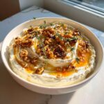 A bowl of creamy whipped ricotta dip topped with candied walnuts, honey drizzle, and fresh thyme sprigs.