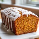 A whole loaf of moist, orange sweet potato pound cake topped with a thick white vanilla glaze.