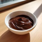 A small white bowl filled with rich, glossy, dark chocolate dip, sitting on a wooden surface.
