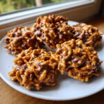 Four delicious haystack cookies made with chow mein noodles and chocolate, resting on a white plate.