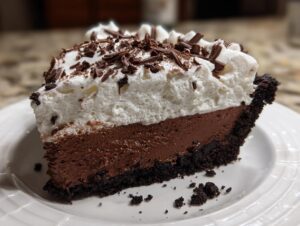 A thick slice of rich chocolate mud pie with a dark crust, chocolate mousse filling, whipped cream, and chocolate shavings.
