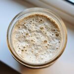 Overhead view of an active sourdough starter, showing a thick layer of foam and bubbles, indicating readiness.