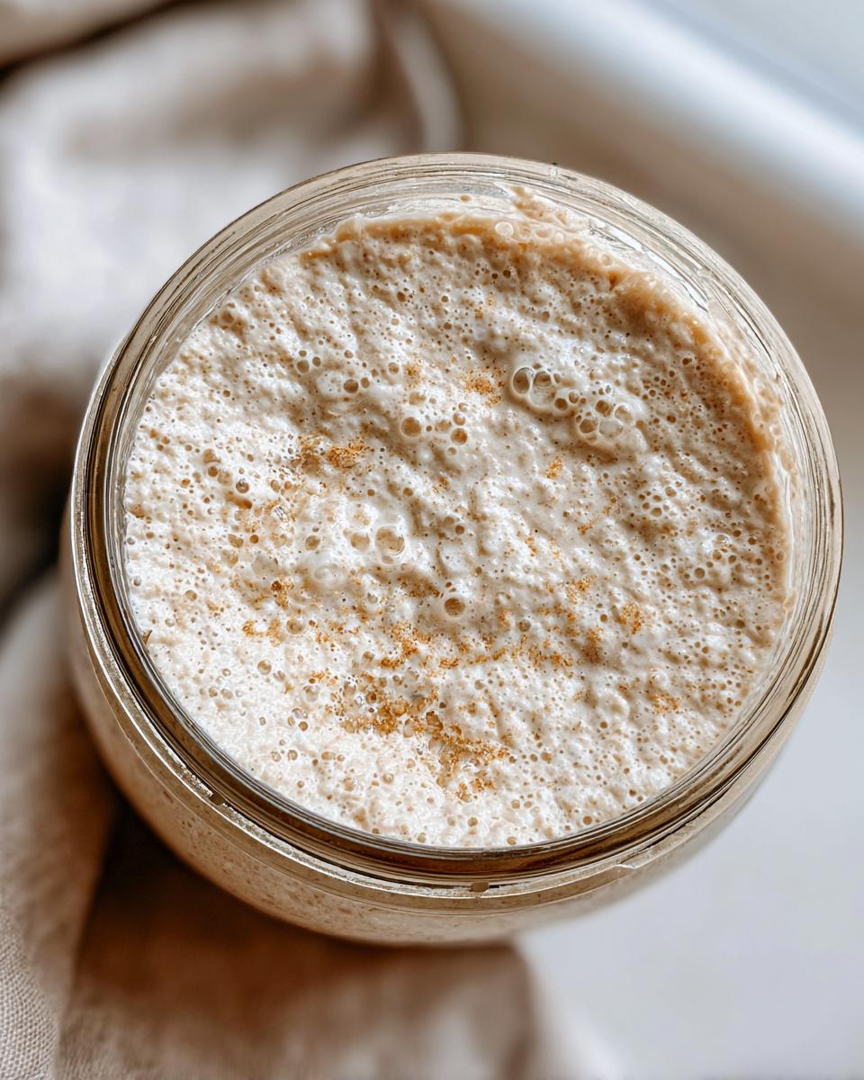 Overhead view of a very active sourdough starter, full of bubbles and slightly peaked in a glass jar.
