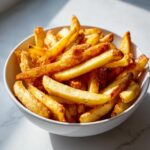 A close-up of golden brown, crispy air fryer french fries piled high in a white bowl.