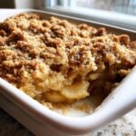 A close-up view of a freshly baked apple crumble with a thick, golden-brown, crumbly topping and soft, saucy apples underneath.