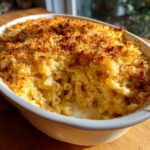 A scoop has been taken out of a creamy baked mac and cheese dish, revealing the cheesy interior and golden brown breadcrumb topping.