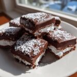 Close-up of several chocolate-covered cool whip candy squares dusted with powdered sugar.