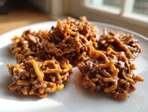 Several rich, chocolate-coated haystack cookies made with chow mein noodles or crispy cereal, sitting on a white plate.