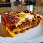 A thick, perfectly baked slice of homemade lasagna showing layers of meat sauce and cheese, topped with melted mozzarella.