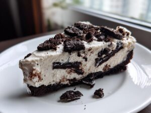A decadent slice of no-bake Oreo pie with a creamy filling and dark chocolate cookie crust, topped with crushed cookies.