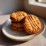 A stack of four golden brown peanut butter cookies with classic crosshatch fork marks, resting on a ceramic plate.