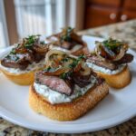 Three pieces of steak crostini topped with creamy sauce, medium-rare steak, and caramelized onions, ready to serve.