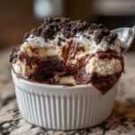 Close-up of a spoonful being taken from a Baileys Chocolate Cheesecake Trifle layered with cream, chocolate sauce, and cookie crumbs.