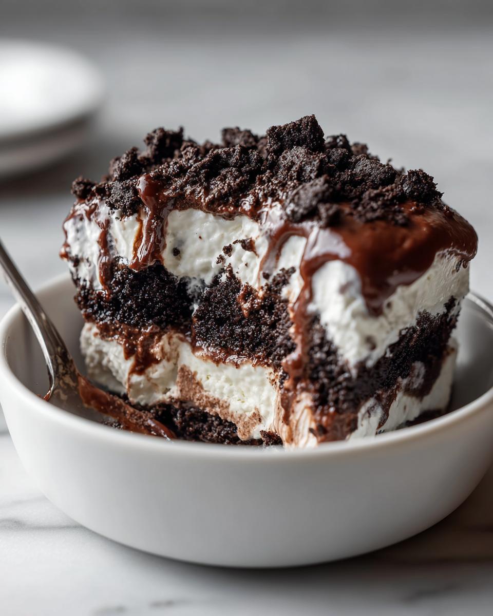 A rich slice of Baileys Chocolate Cheesecake Trifle layered with dark cake, cream, and topped with chocolate drizzle and crumbs.
