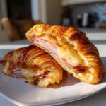 Two halves of a golden brown baked ham and cheese croissants, showing melted cheese oozing out.