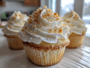 A close-up of a beautifully frosted banana pudding cupcake topped with crushed wafer crumbs.