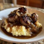A close-up of rich bangers and mash topped with caramelized onion gravy.