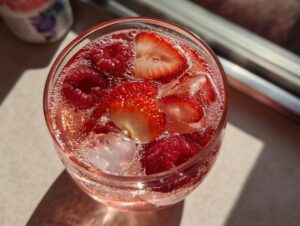Close-up overhead view of a glass filled with pink champagne punch, ice cubes, sliced strawberries, and whole raspberries.