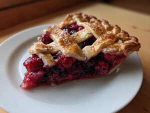 A close-up of a glistening slice of berry pie featuring a flaky lattice crust and vibrant red berry filling.