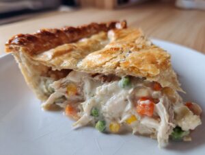 Close-up of a slice of turkey pot pie recipe showing creamy filling, shredded turkey, peas, and carrots under a golden, flaky crust.