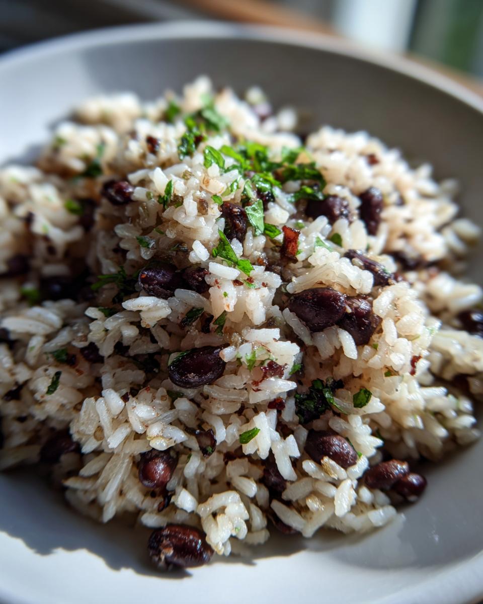 A close-up, bright photo of fluffy white rice mixed with dark black beans and topped with fresh green herbs, showcasing the black beans and rice dish.