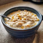 A close-up of a hearty bowl of creamy white cream cheese chicken chili, featuring shredded chicken, corn, and white beans.